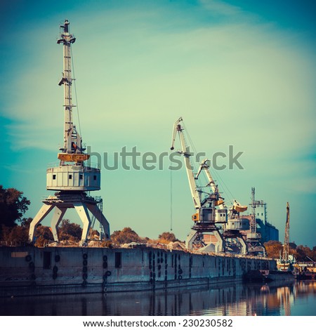 Working cranes for cargo at the shipyard docks in river port, vintage stylized.
