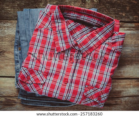 Plaid shirt and pair of jeans on wooden background. Top view. Vintage stylized.