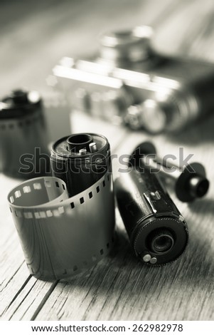 Old photo film rolls, cassette and retro camera on background. Black and white stylized.