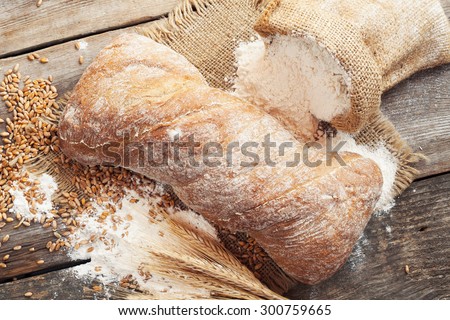 Fresh homemade bread, sack of flour and wheat ears on rustic wooden table.