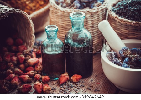 Bottles of tincture, basket with rose buds, and dried forget me not flowers in mortar. Herbal medicine. Selective focus.