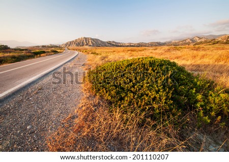 Dry tarmac road with the turf, dry grass and mountains in background in inland of Rhodes island in Greece