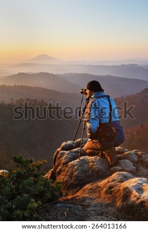 Photographer with tripod taking pictures on the top of the hill above the misty valley and the beautiful view during the sunrise in national park Bohemian Switzerland