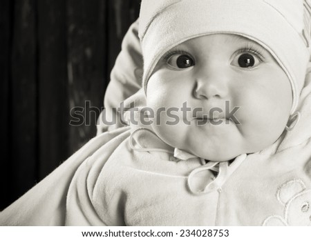 Portrait of a baby with big brown eyes and a big round cheeks, wearing a hat on his head.