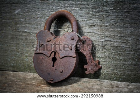 The old rusty padlock with keys lying on textured wooden boards.