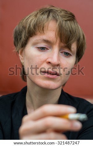 A woman is sitting in a very depressed mood, in the hand between the fingers lit cigarette.
