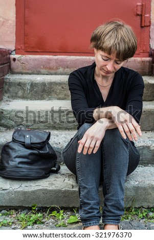 A woman sits on the concrete stairs in a very depressed mood, lying next to her on the stairs of her backpack.