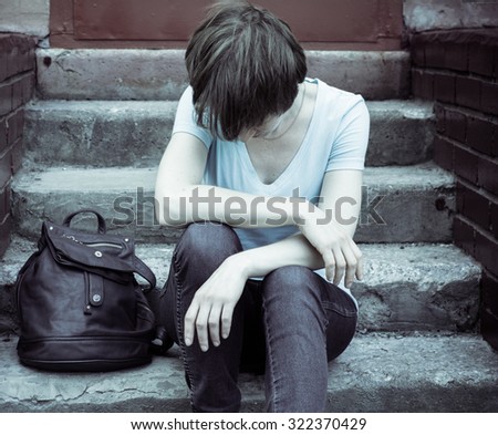 A woman sits on the concrete stairs in a very depressed mood, lying next to her on the stairs of her backpack.