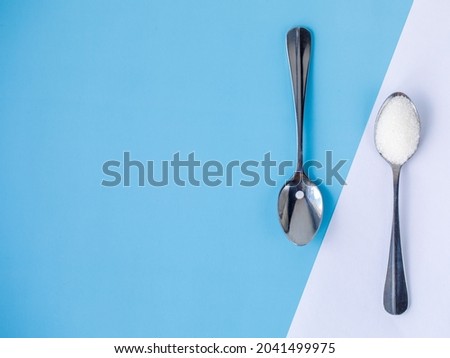 Choice of Sweetener in tablets or regular sugar. Alternative to sugar for diabetics. Sugar-replacement tablet and sugar in tea spoons lying in opposite directions on diagonal blue white background