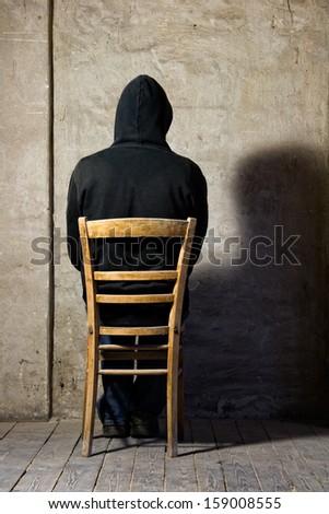 man with hooded jacket sitting in front of an old wall