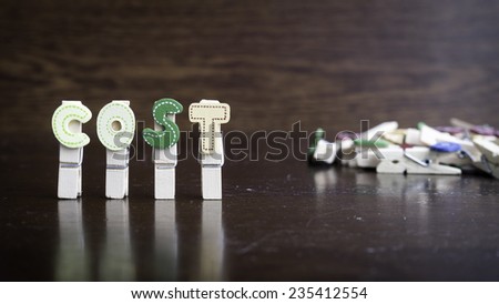 Common business terms - Slightly defocused and close-up of COST word on clothes peg stick with lots of clothes peg at background