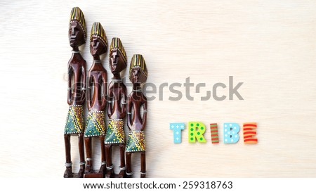 Decorative Asian or African tribal totem carved from forest wood with letter Tribe on clean wooden surface. Concept of aboriginal art. Slightly defocused and close-up shot. Copy space.