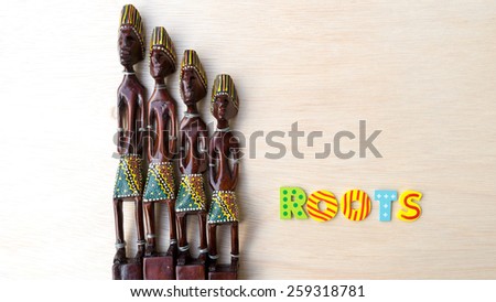Decorative Asian or African tribal totem carved from forest wood with letter ROOTS on clean wooden surface. Concept of aboriginal art. Slightly defocused and close-up shot. Copy space.