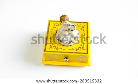 Yellow colour winding music or jewellery box case with white cute angelic cupid statue playing musical item on top. Isolated on white background.