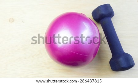 Mini dumbbell or dumb bell with pilates toning ball for workout activities on wooden surface. Concept of gym basic exercise fitness equipment. Copy space.