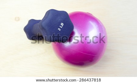 Mini dumbbell or dumb bell with pilates toning ball for workout activities on wooden surface. Concept of gym basic exercise fitness equipment. Copy space.
