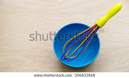 Colourful cute plastic whisk or egg beater and blue bowl on empty wooden surface. Concept of kitchen tool for kids or young chef. Slightly de-focused and close-up shot. Copy space.