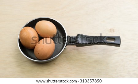 Black color metal mini frying pan and few chicken eggs on wooden table surface. Concept of breakfast cooking utensil. Slightly de-focused and close-up shot. Copy space.