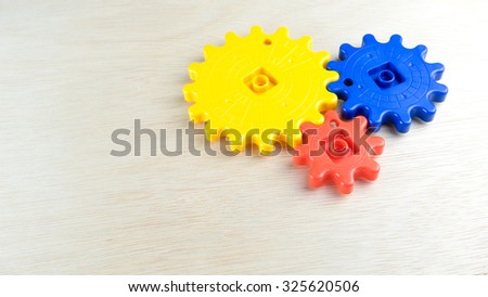 Cute and multicolor plastic gears or cogwheel on wooden surface. Concept of process and rotating mechanism. Slightly de-focused and close-up shot. Copy space.