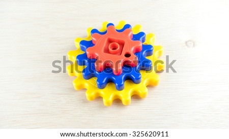 Cute and colourful plastic gears or cogwheel on wooden surface. Concept of process and rotating mechanism. Slightly de-focused and close-up shot. Copy space.