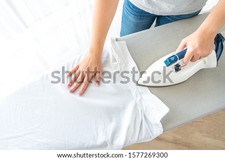 Female hands ironing white shirt collar on ironing board, view from above