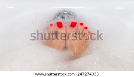 Feet with red nails soaking in spa bath with copy space
