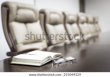 Closeup of notebook and glasses on table in empty corporate conference room before business meeting in office