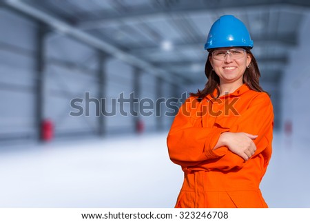 Woman worker in orange overall and blue safety helmet on storehouse background