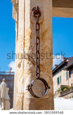 A metal neck iron on a pillory made of stone, which hangs down from a chain and where in former times prisoners were chained, who were put on the pillory Stockfoto © 