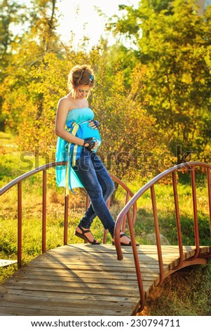 Young attractive pregnant girl with an unusual make-up standing on the bridge at sunny day
