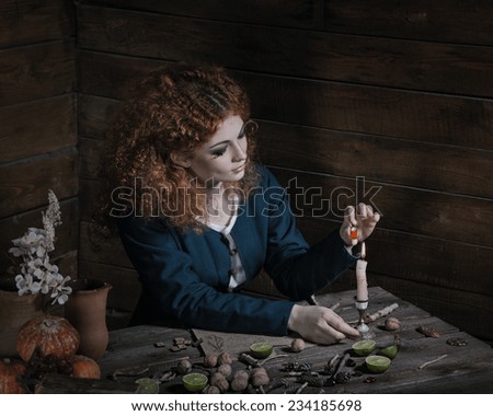 The red-haired witch preparing a potion from a variety of ingredients, spread on a wooden table. Picture toned.