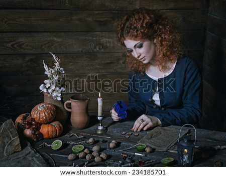 The red-haired witch preparing a potion from a variety of ingredients, spread on a wooden table. Picture toned.