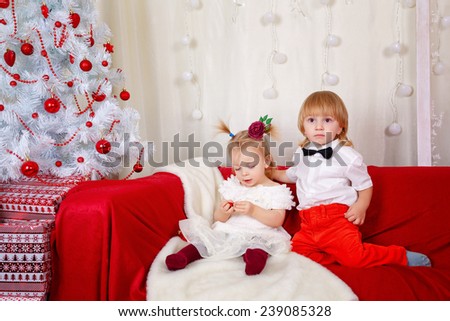 Little brother and sister sitting on the couch near Christmas tree