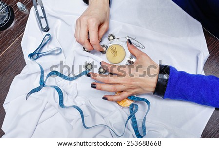 Hands of woman designer at work on the desk. Fabric, buttons and needles on the table. Person is not recognizable.