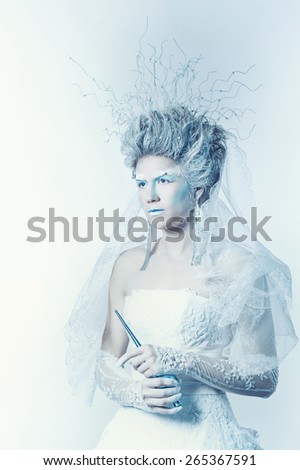 Mysterious and unusual girl with face art in the form of the Snow Queen. Girl dressed in a white dress and has a high hairstyle. Fairy holding a wand. The concept of the kingdom of cold.