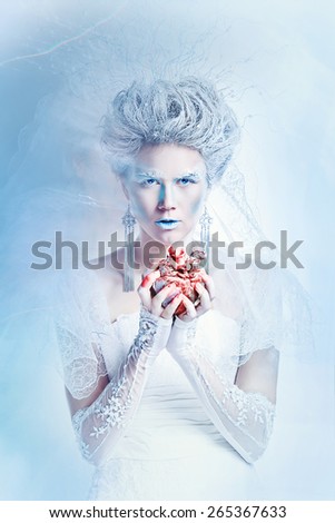 Mysterious and unusual girl with face art in the form of the Snow Queen. Girl holding a human heart in the blood. The concept of eternal winter.