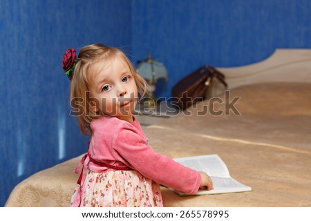 Little cute girl reading a book in the bedroom. The concept of education in the preschool years.
