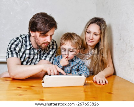 Young family. Mother, father and son looking at a tablet pc while sitting at the kitchen table. Father shows his finger on the touchscreen. Happy childhood.