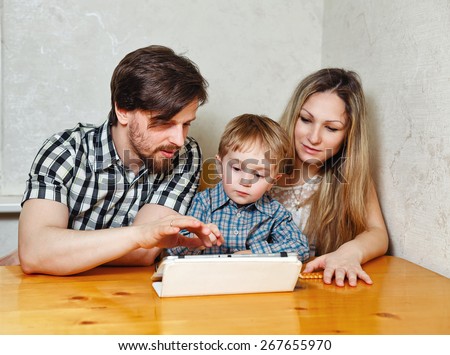 Young family. Mother, father and son looking at a tablet pc while sitting at the kitchen table. Father and child shows a finger on the touchscreen. Happy childhood.