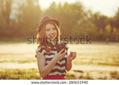 Young attractive girl in a hat holding a cell phone. The concept of urban street youth fashion.