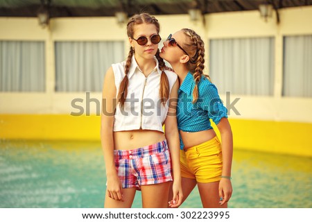Teen girl in sunglasses standing near the fountain in summer park. Girls dressed in shorts and a shirt. On summer vacation. The concept of true friendship.