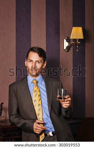 Successful businessman holding a glass of whiskey. Man celebrates good deal. Vintage background. Leadership concept.