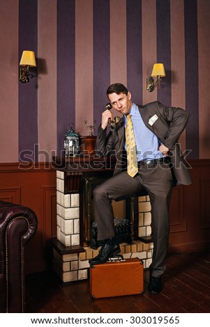 Successful businessman speaks by phone. The man put his foot on suitcase. Business travel. Vintage background. Leadership concept.