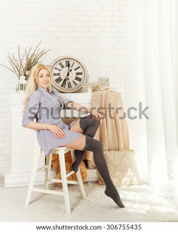 Cute blonde girl in stockings sitting on a chair by the fireplace. The concept of home comfort.