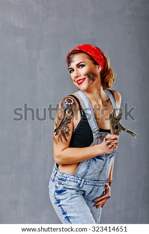 Young girl in denim overalls mechanic holding a hand vise. Professional work. Face art. Jack of all trades. The concept of the girl has been a man\'s job.