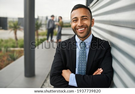 Young smiling business university student standing against college campus wall with arms crossed