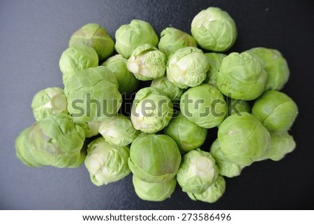 A pile of fresh green Brussels sprouts on dark surface. Healthy/clean eating concept; organic/unprocessed food; paleo diet.