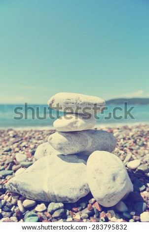 Stack of white stones balancing on the pebbly beach, on a sunny day. Image filtered in faded, washed out, retro style; summer vintage concept. Concept of balance, harmony and well-being.