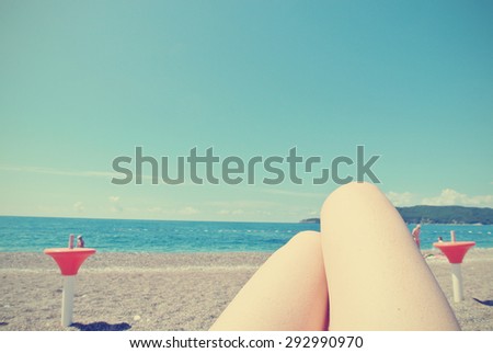 Legs (knees) of a young woman sunbathing on the beach, on a sunny day. Filtered image in faded, washed out, retro style; summer vintage concept. Can be used as a background. Personal perspective.