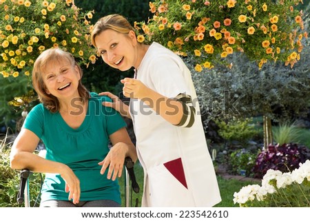 Senior and their nurse standing in the garden and pointing at camera